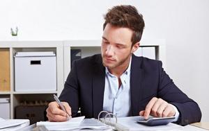Mann sitzt mit Taschenrechner und Akten im Büro am Schreibtisch
